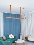 Clérachic tan strap pendant above a living room with a green sofa, blue curtains and a daisy-shaped cushion.