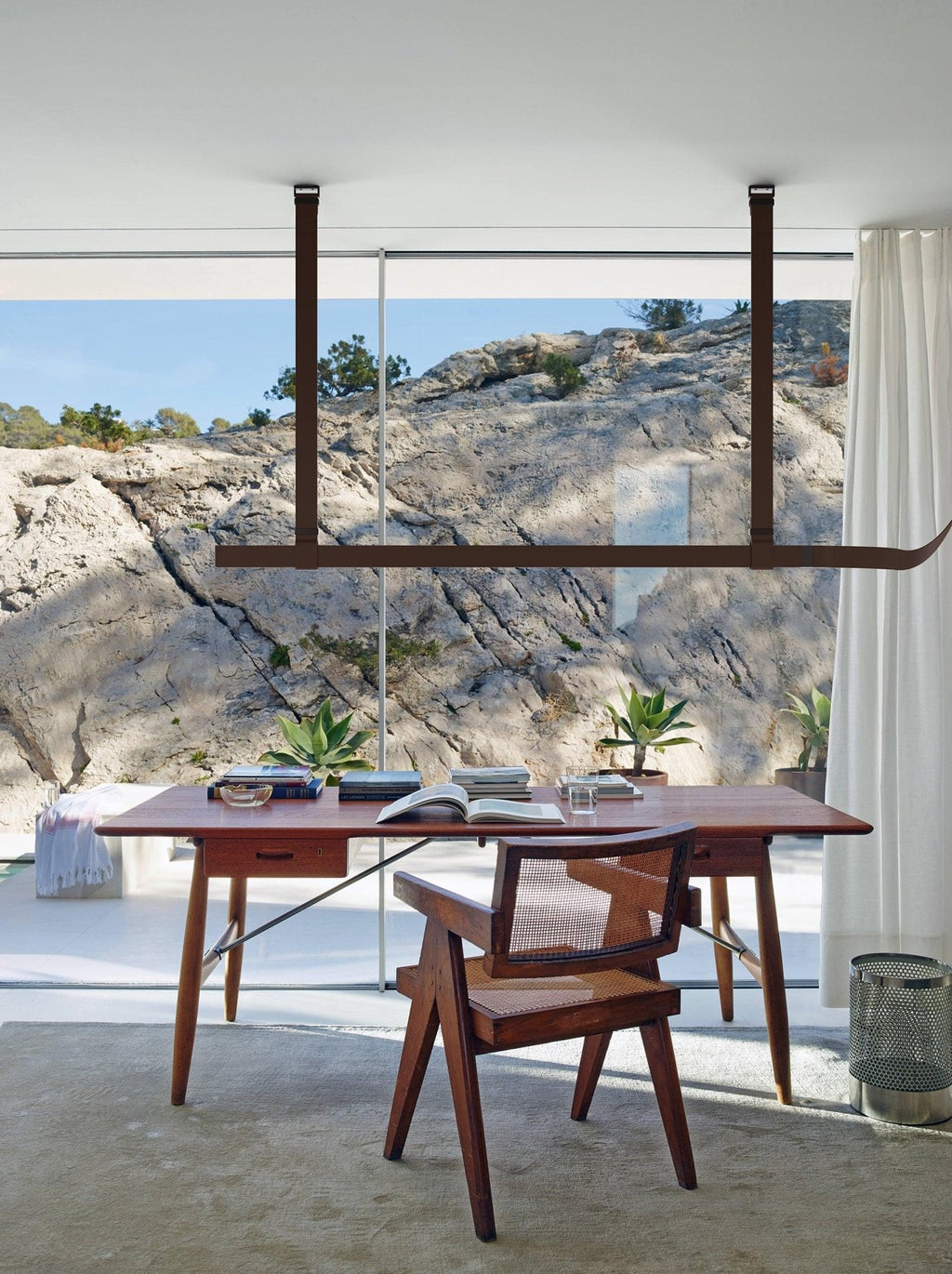 Brown leather strap pendant hung in front of a wide window with a rocky view, above a wooden desk, from Clérachic.