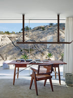 Brown leather strap pendant hung in front of a wide window with a rocky view, above a wooden desk, from Clérachic.