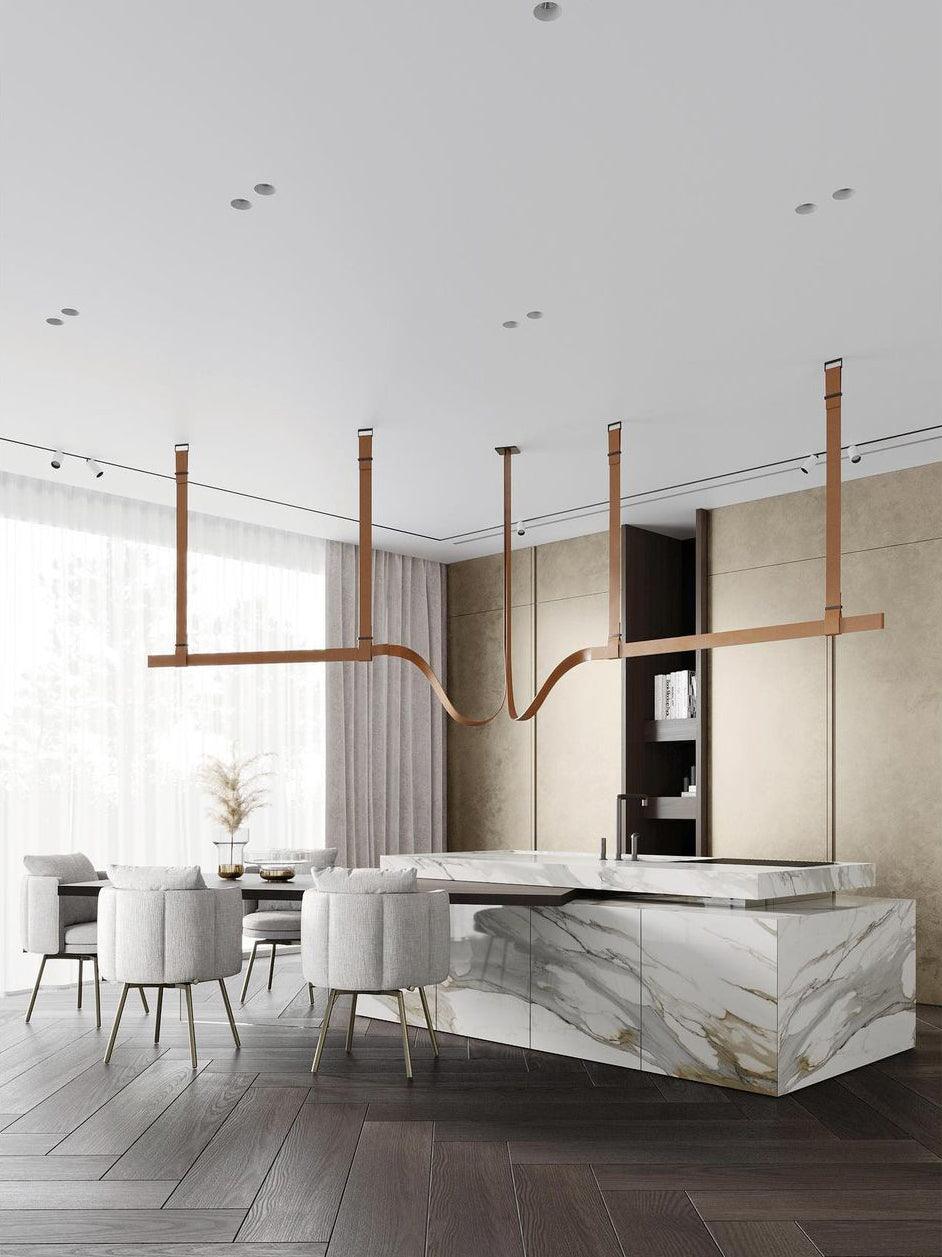 Tan strap pendants carrying light bars above a marble kitchen island and round upholstered chairs, from Clérachic.