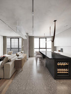 A strap pendant hangs in the middle of a long, bright room with a sofa, a black island and floor-to-ceiling windows, from Clérachic.