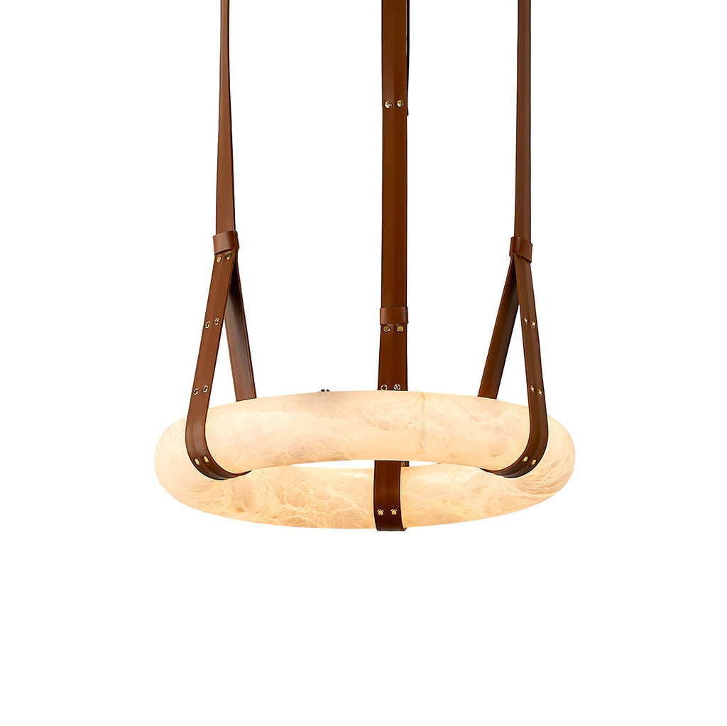 Clérachic's leather-strap ring chandelier seen close up, brown belts riveted in brass cradling the glowing alabaster ring.