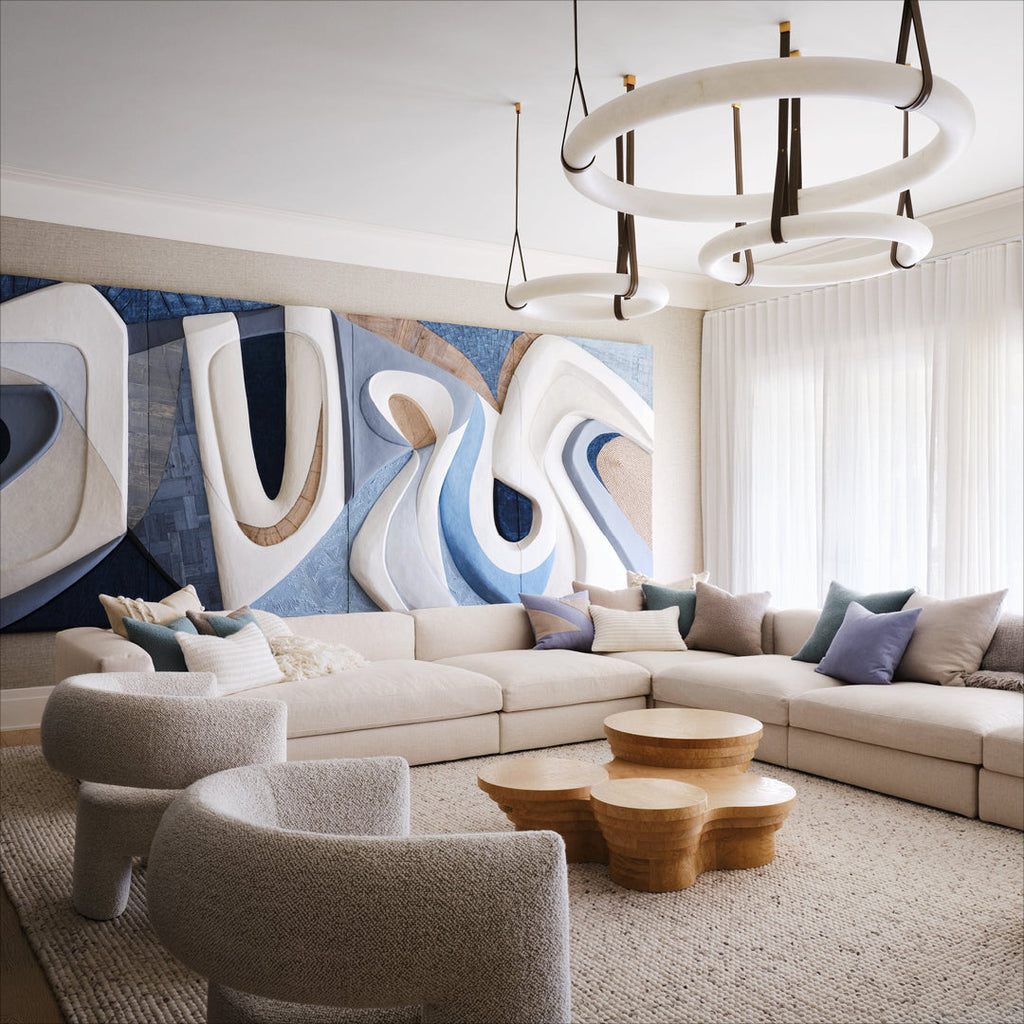 Two Clérachic alabaster ring chandeliers hung at staggered drops over a pale sectional sofa and a blue relief artwork.