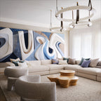 Two Clérachic alabaster ring chandeliers hung at staggered drops over a pale sectional sofa and a blue relief artwork.