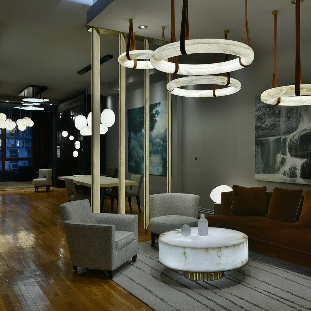 Four Clérachic alabaster ring chandeliers glowing at staggered heights above a dim evening lounge with velvet seating.
