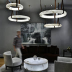 Clérachic alabaster ring chandeliers in two interlocking pairs lighting a grey lounge as a guest walks past the artwork.