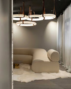 A cluster of Clérachic alabaster ring chandeliers lighting a curved cream sofa and sheepskin rug in a showroom setting.