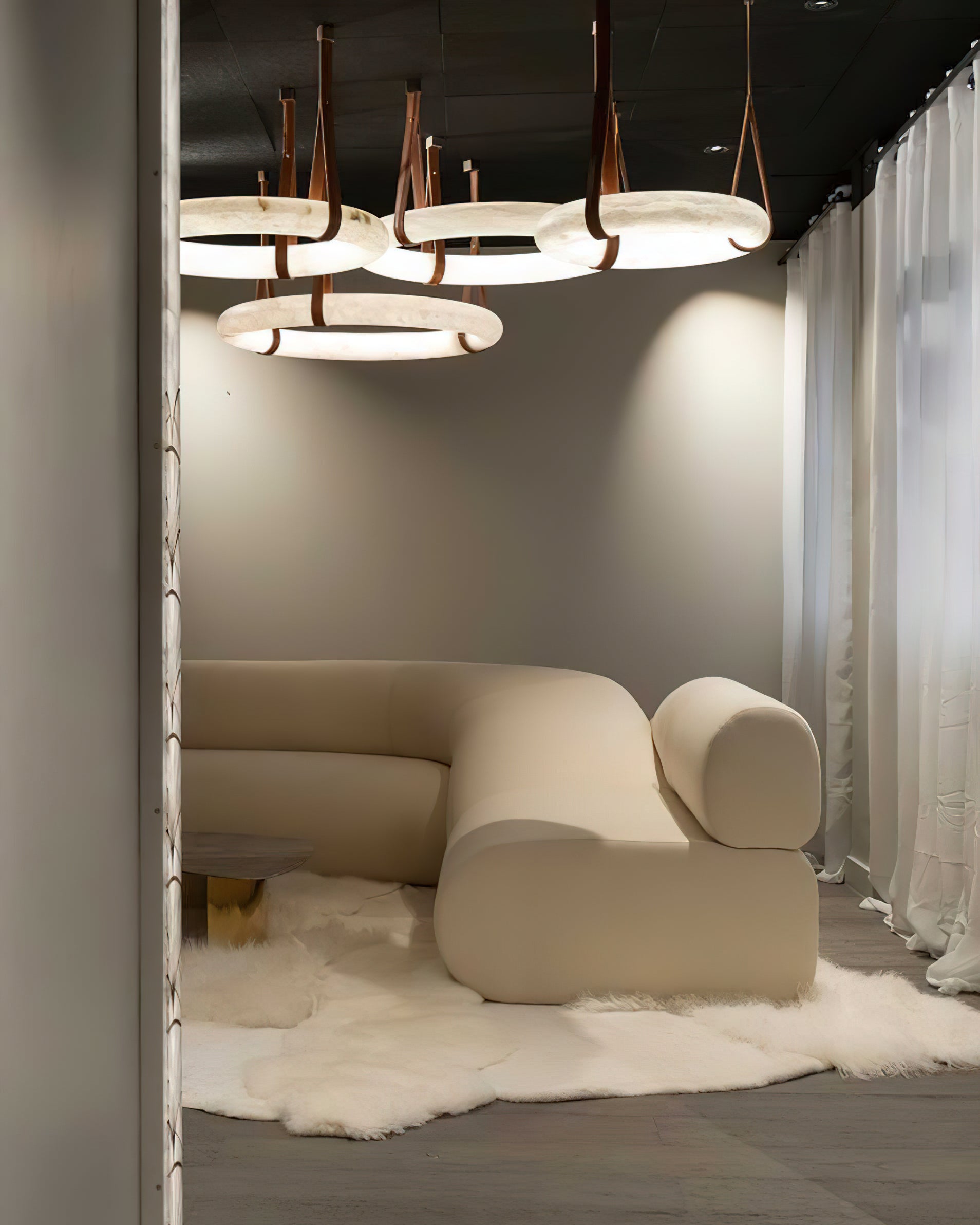 A cluster of Clérachic alabaster ring chandeliers lighting a curved cream sofa and sheepskin rug in a showroom setting.
