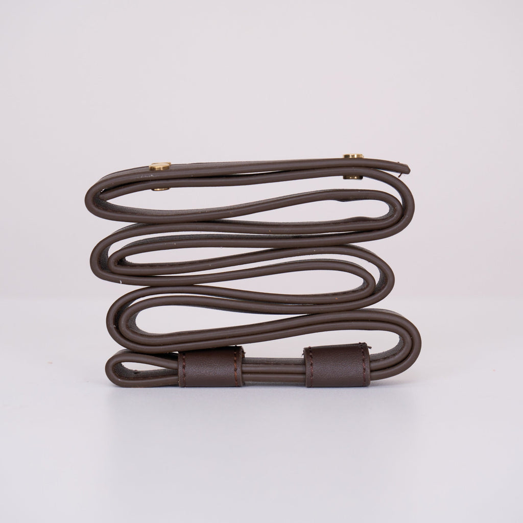 The dark brown Clérachic suspension belt coiled side on, showing its stitched keeper loop and paired brass screw heads.