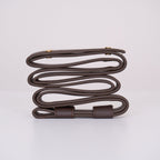 The dark brown Clérachic suspension belt coiled side on, showing its stitched keeper loop and paired brass screw heads.