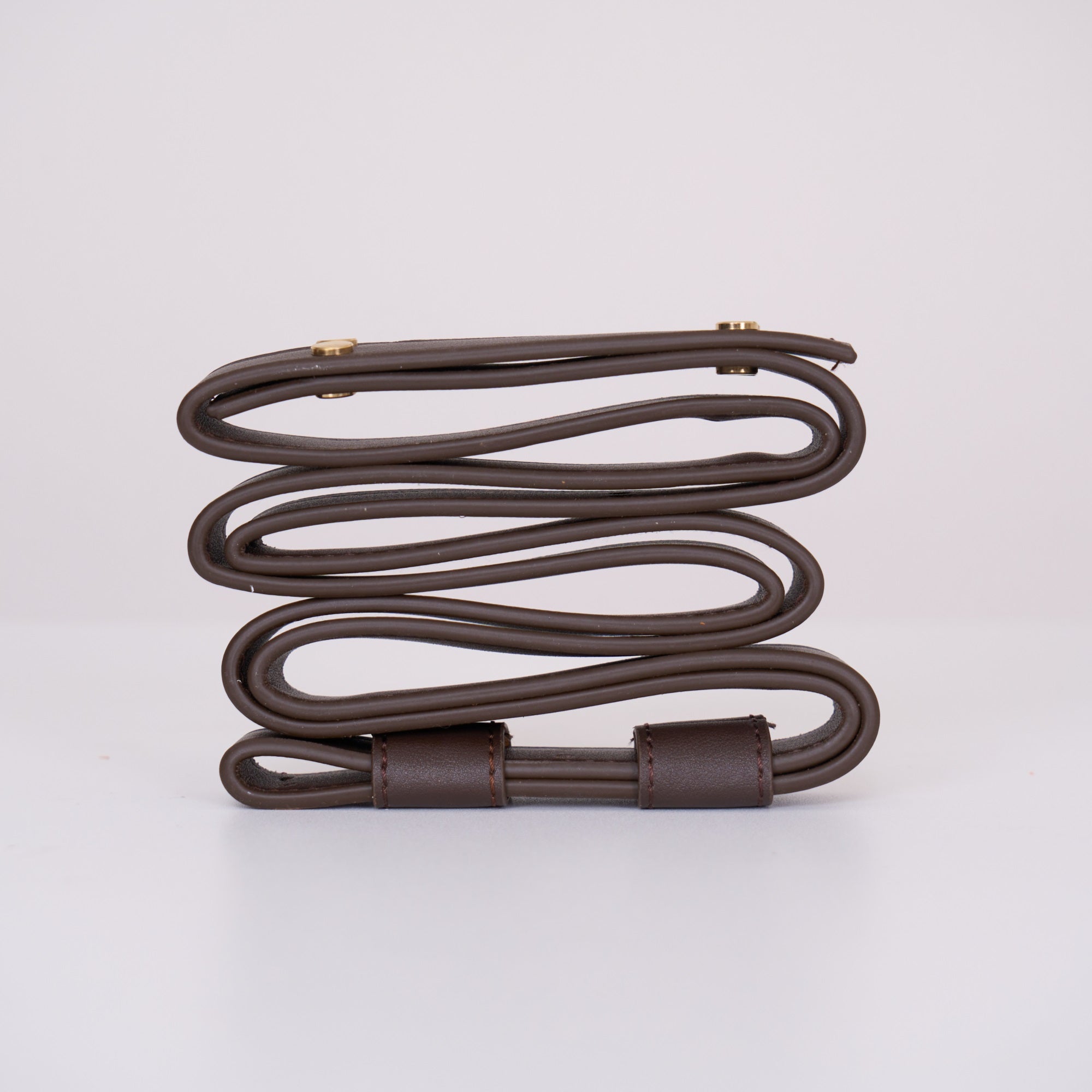 The dark brown Clérachic suspension belt coiled side on, showing its stitched keeper loop and paired brass screw heads.