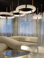 Several Clérachic alabaster ring chandeliers overlapping above a cream sofa in a daylit room with sheer full-length curtains.