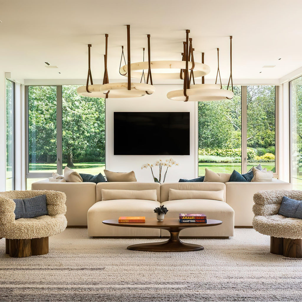 A Clérachic alabaster ring chandelier cluster over a cream sectional in a garden-facing living room with full height glass.