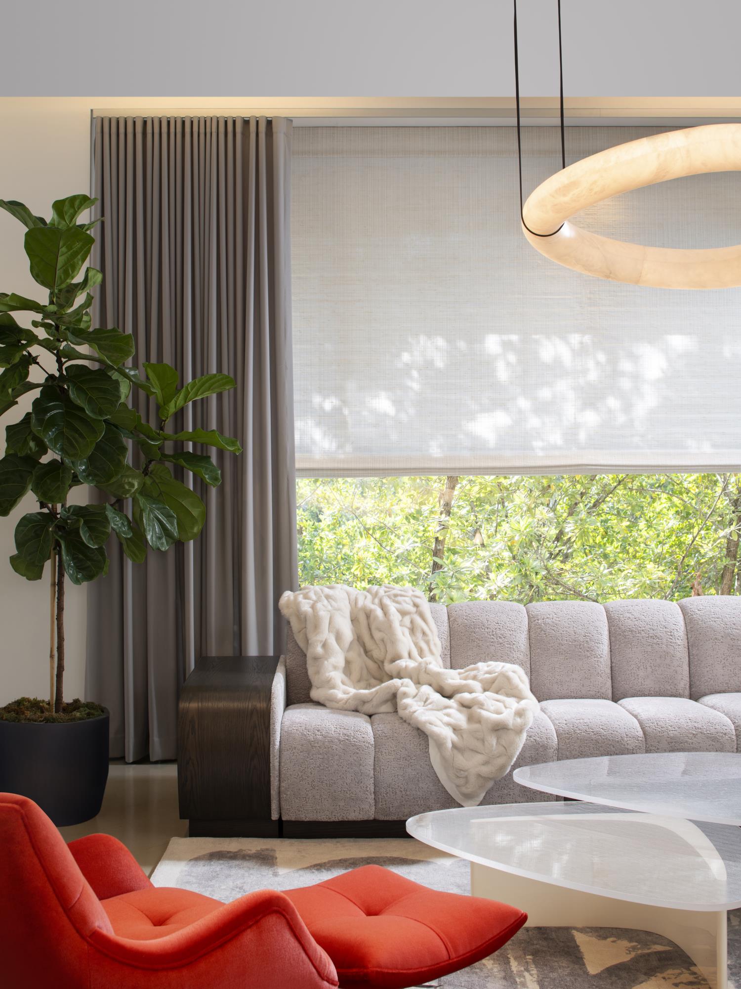 A Clérachic alabaster ring chandelier glowing at the frame edge above a boucle sofa, red lounge chair and fiddle-leaf fig.