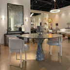 A Clérachic alabaster ring chandelier lit over a round marble dining table on a furniture showroom floor.