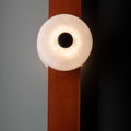 Detail of the Clérachic Leather Strap Wall Sconce, its alabaster disc washing warm light across a cognac leather strap.