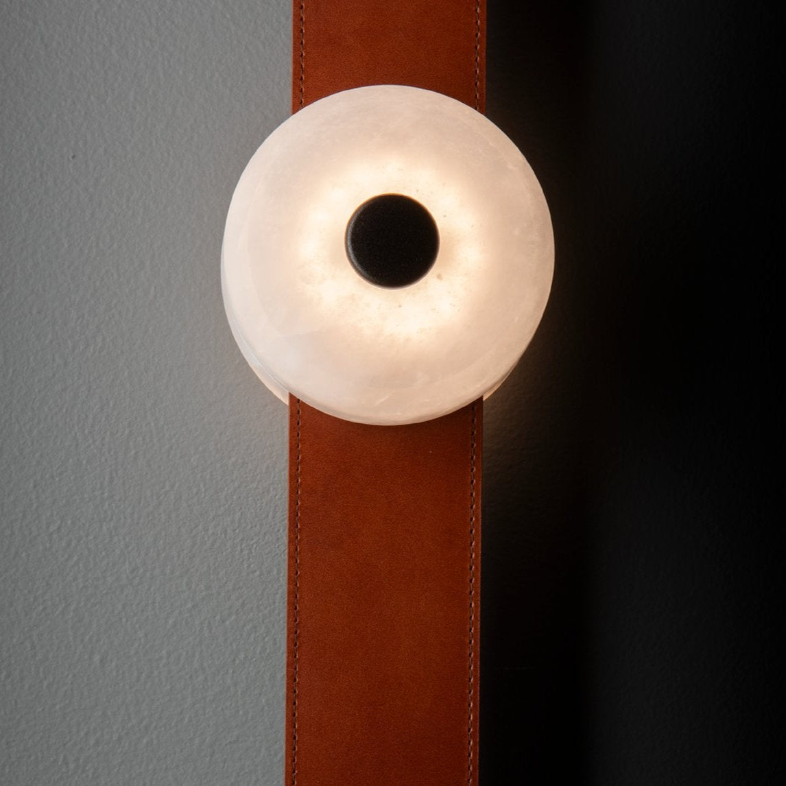 Detail of the Clérachic Leather Strap Wall Sconce, its alabaster disc washing warm light across a cognac leather strap.