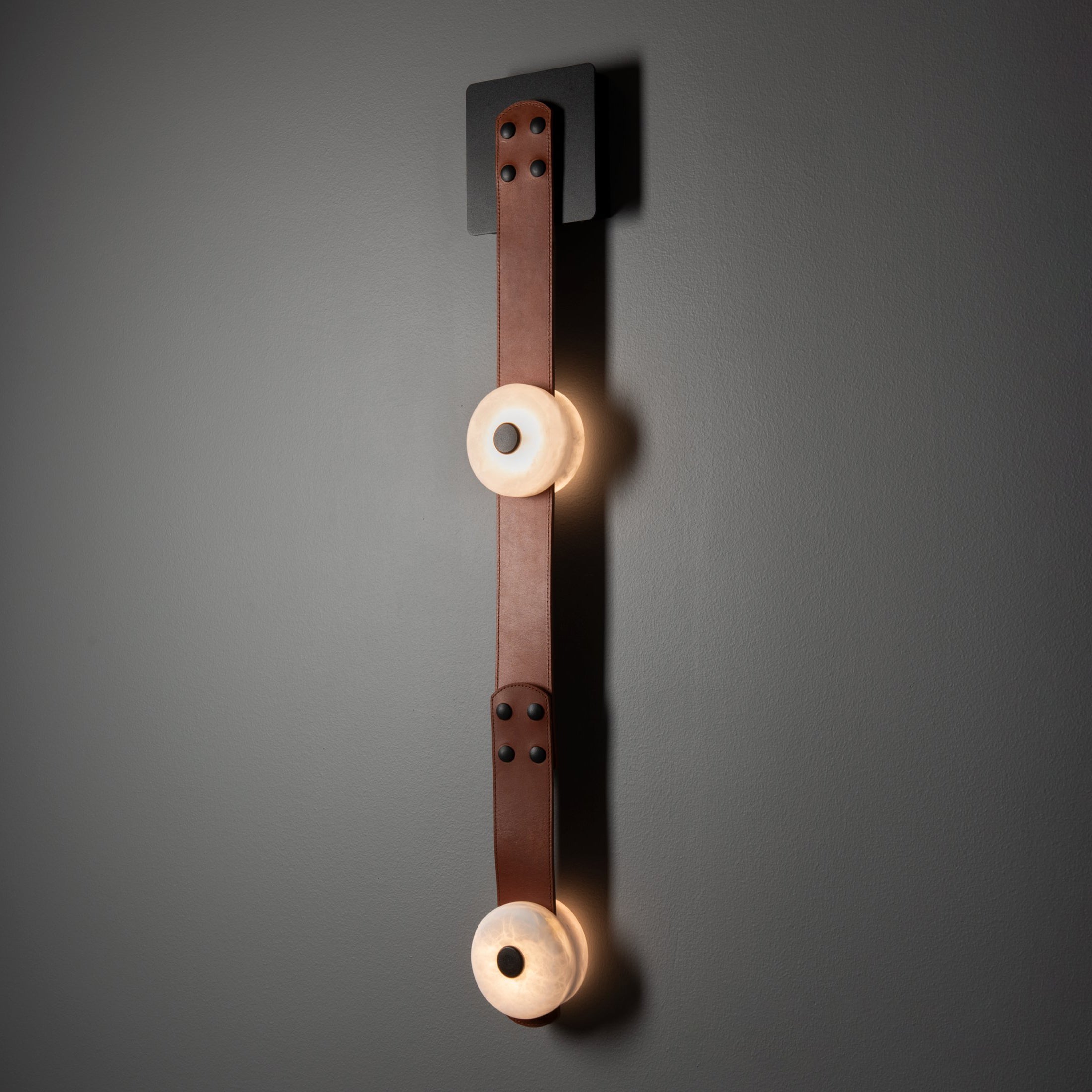 The two-head Clérachic Leather Strap Wall Sconce in cognac leather, two alabaster discs spaced down a riveted strap.
