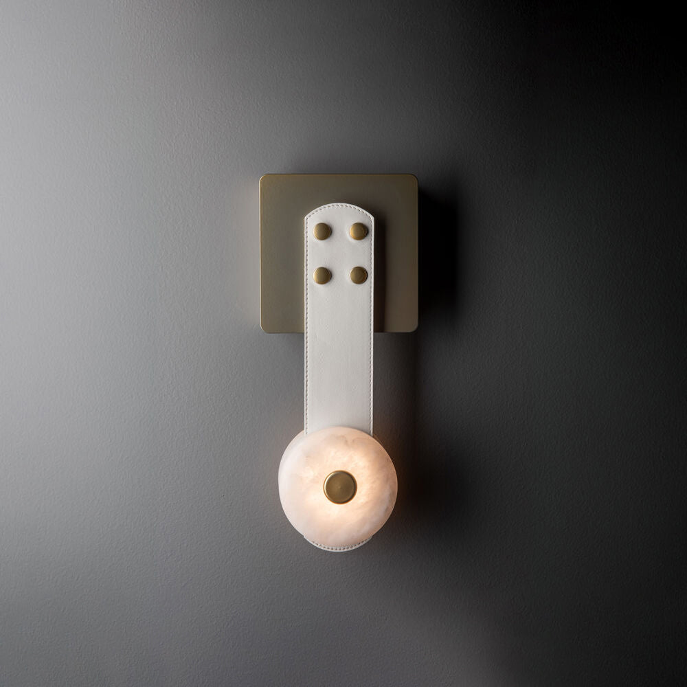White leather and brass on the Clérachic Leather Strap Wall Sconce, the short strap dropping to one lit alabaster disc.