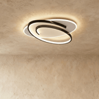 Clérachic oval flush ceiling light with a swirling black frame around a glowing white diffuser, on a limewash ceiling.