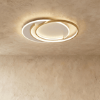 Clérachic flush ceiling light of gold aluminium rings in a crescent layout, glowing warm on a limewash ceiling.