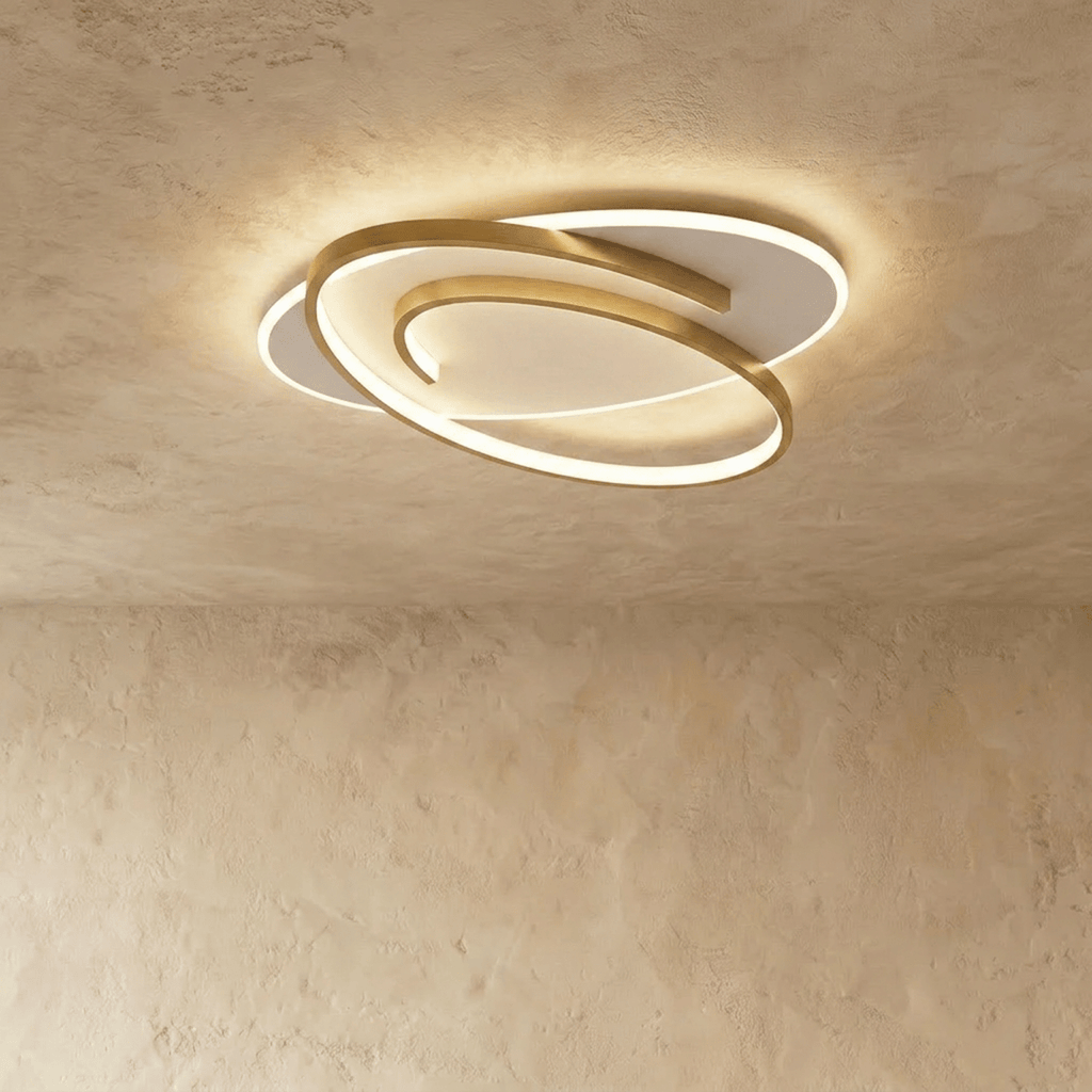 Clérachic oval flush ceiling light with a swirling gold frame around a glowing white diffuser, on a limewash ceiling.