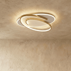Clérachic oval flush ceiling light with a swirling gold frame around a glowing white diffuser, on a limewash ceiling.