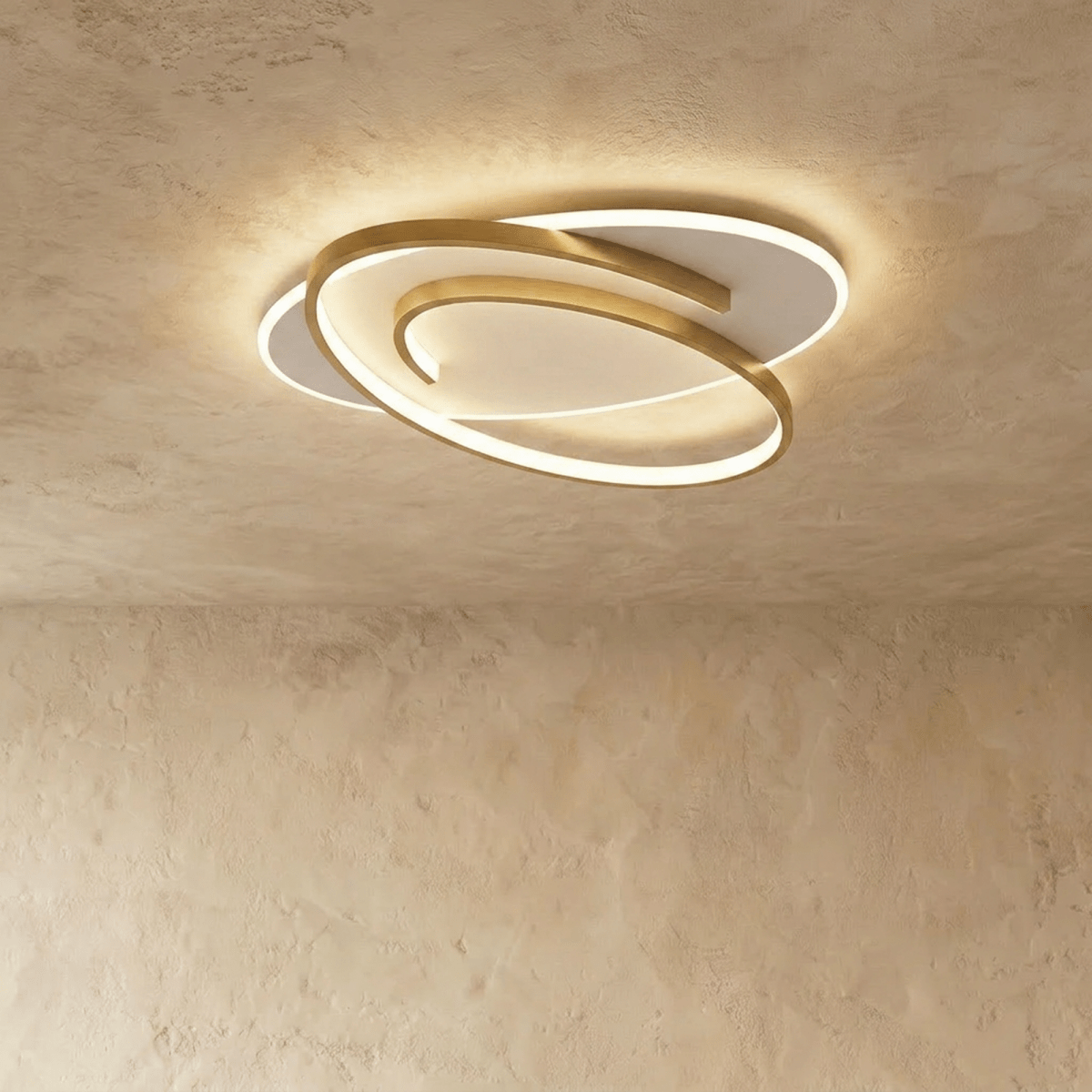 Clérachic oval flush ceiling light with a swirling gold frame around a glowing white diffuser, on a limewash ceiling.