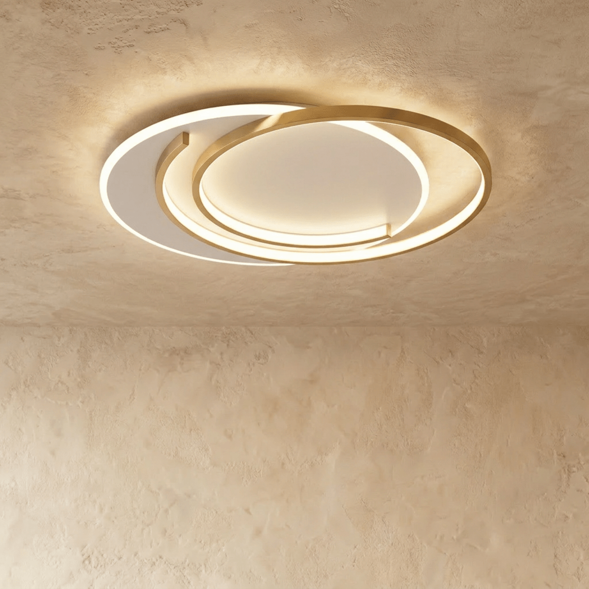 Clérachic wider flush ceiling light with gold crescent-layout rings and a lit white diffuser on a limewash ceiling.