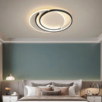 Clérachic black crescent-ring ceiling light over a bed with a sage wall, plus a small glass pendant at the side.
