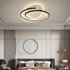 Clérachic swirling black-frame ceiling light above a grey upholstered bed in a room with wall art and a gold-ringed panel.