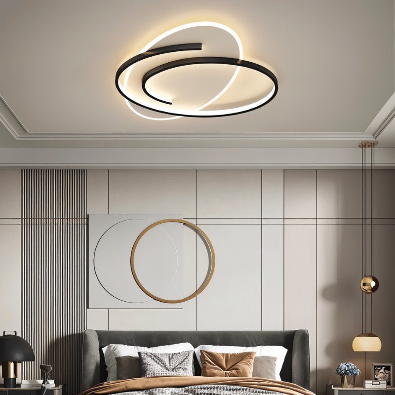 Clérachic swirling black-frame ceiling light above a grey upholstered bed in a room with wall art and a gold-ringed panel.