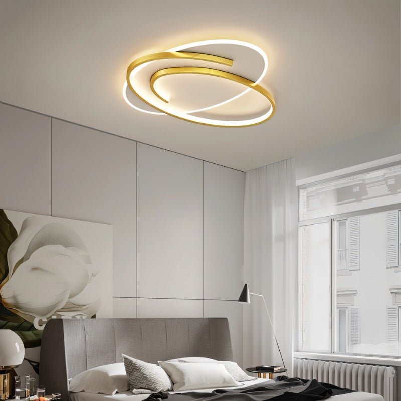 Clérachic oval ceiling light with a swirling gold frame above a grey bed, tall window and white curtain.