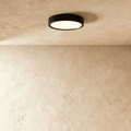 Clérachic slim round black LED downlight lit with a soft warm glow, surface mounted on a textured limewash ceiling.