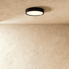 Clérachic slim round black LED downlight lit with a soft warm glow, surface mounted on a textured limewash ceiling.