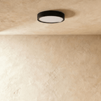 Clérachic slim round black surface-mounted LED downlight switched off, its frosted white diffuser visible on a limewash ceiling.