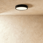 Clérachic mid-size round black surface-mounted LED downlight glowing warm white against a textured plaster ceiling in the studio.