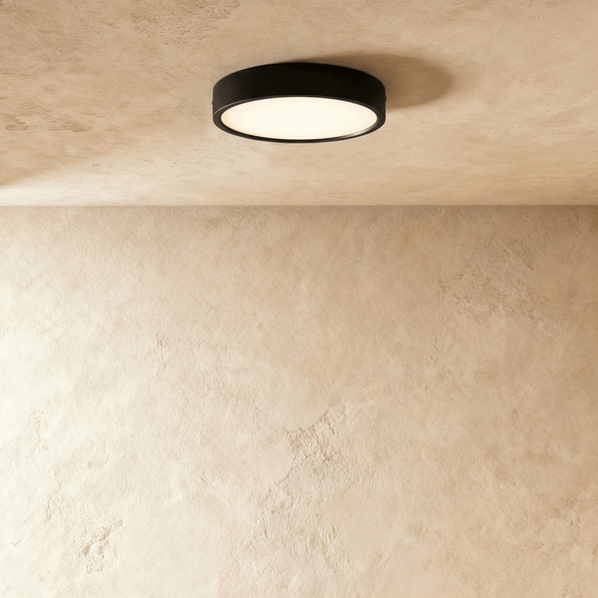 Clérachic mid-size round black surface-mounted LED downlight glowing warm white against a textured plaster ceiling in the studio.