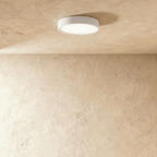 Clérachic slim round white surface-mounted LED downlight glowing softly, mounted flat on a textured limewash ceiling.