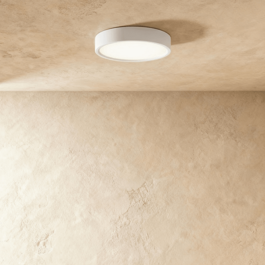 Clérachic mid-size round white surface-mounted LED downlight lit warm white on a textured plaster ceiling in the studio.