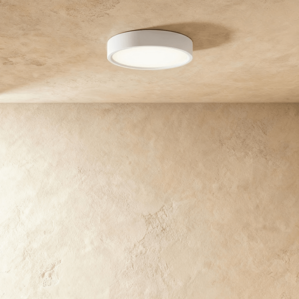 Clérachic mid-size round white surface-mounted LED downlight lit warm white on a textured plaster ceiling in the studio.