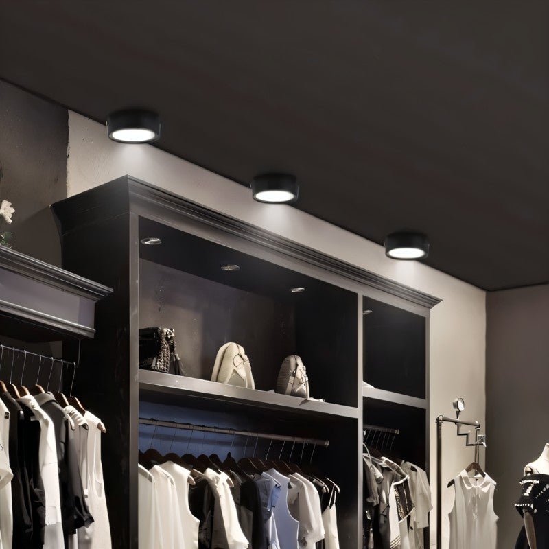 Clérachic row of black round surface-mounted downlights lighting a dressing room with open shelves, shoes and hanging clothes.