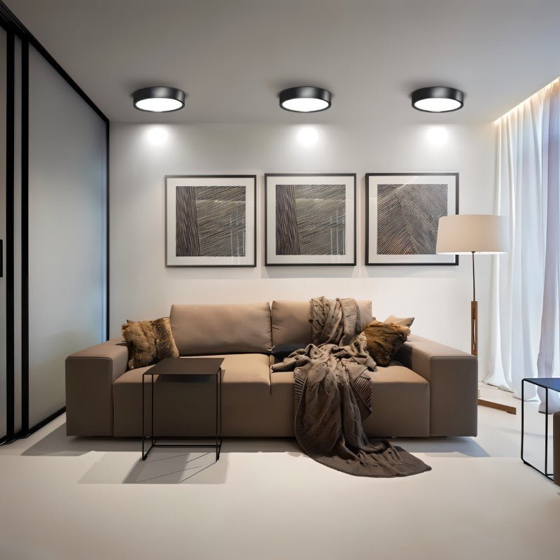 Clérachic three black round surface-mounted downlights above a taupe sofa and framed prints in a calm, bright living room.