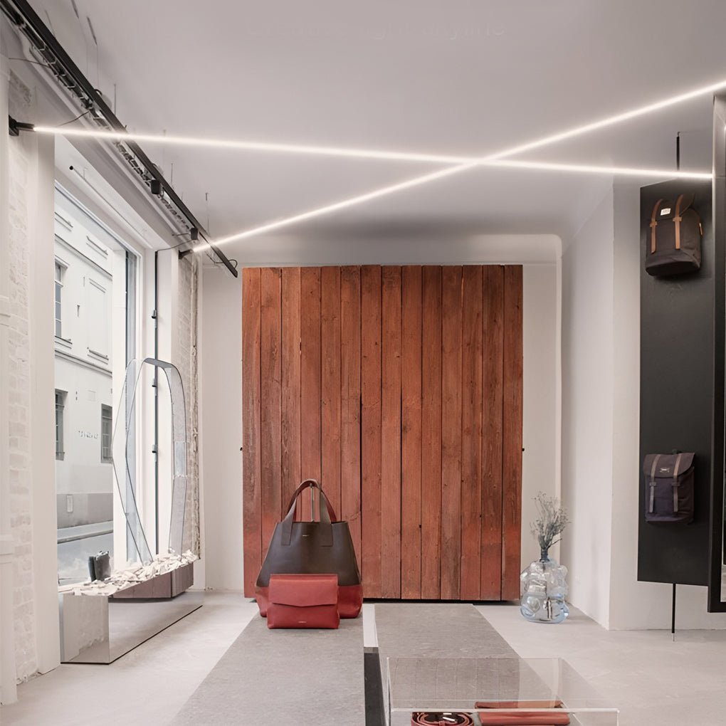 Two Clérachic strip lights cross the ceiling of a bright boutique, above a rust-red wooden wall and a pair of handbags.