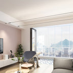 Two thin Clérachic strip lights run along the ceiling of a living room with a pink wall, a grey armchair and a city view.