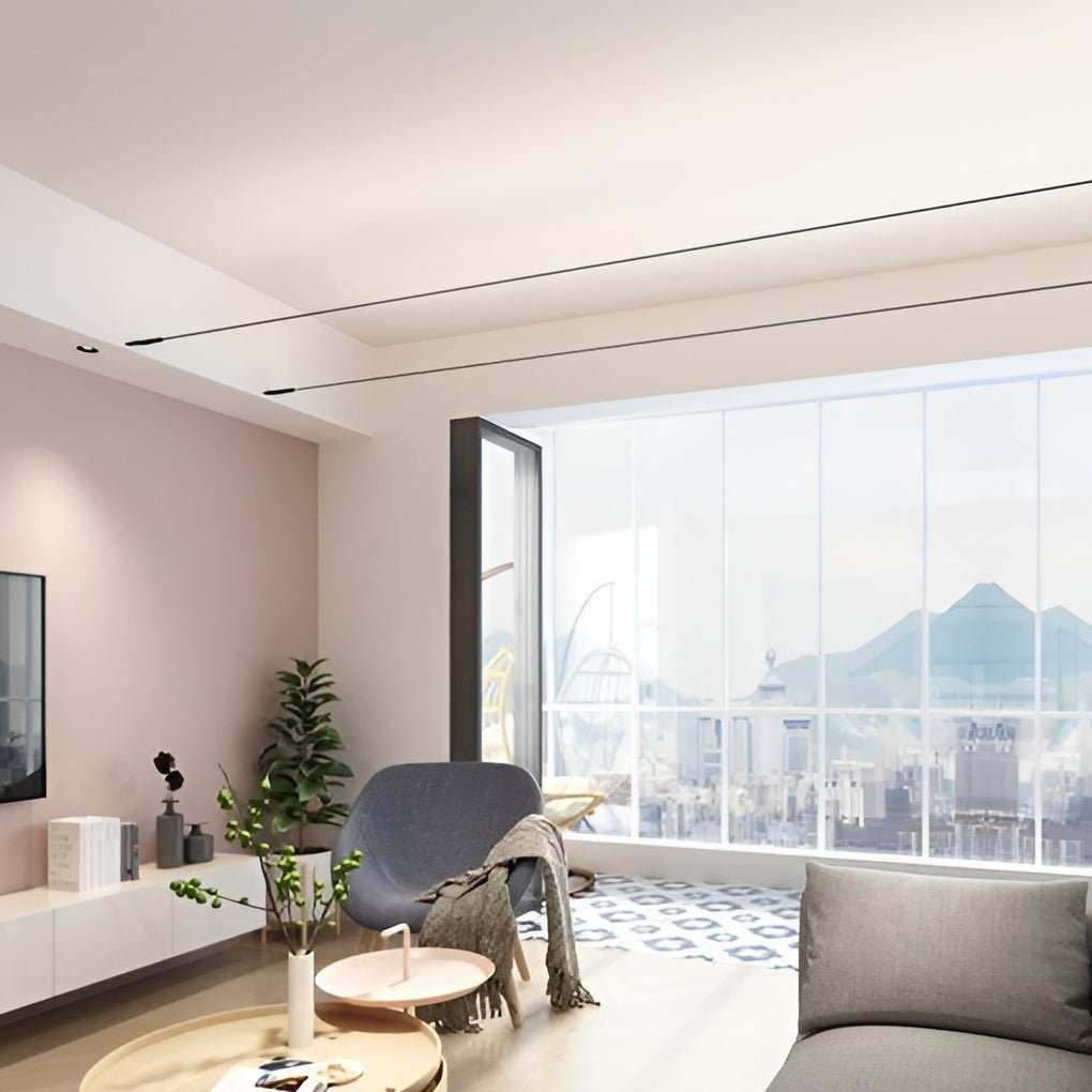 Two thin Clérachic strip lights run along the ceiling of a living room with a pink wall, a grey armchair and a city view.