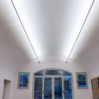 Two long Clérachic strip lights slope up a vaulted ceiling, washing it with bright white light above tall arched windows.
