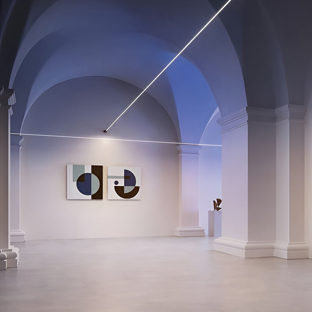 A Clérachic strip light crosses a vaulted gallery hall in a thin white line, with two framed artworks on the far wall.