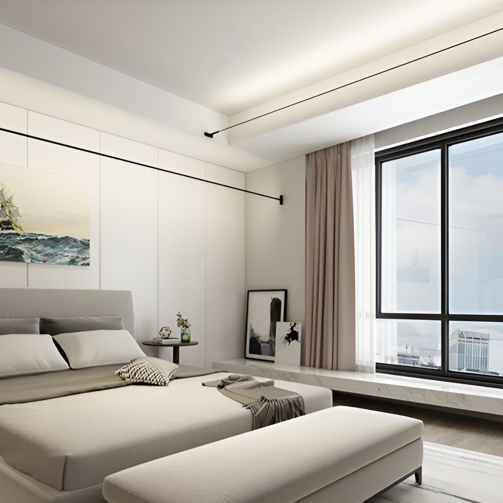 Two Clérachic strip lights run across a bedroom ceiling and wall, above a pale bed and a large window.