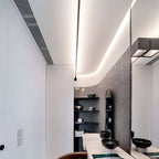 A Clérachic strip light drops from a glowing ceiling curve in a narrow room with dark shelves and a black basin.